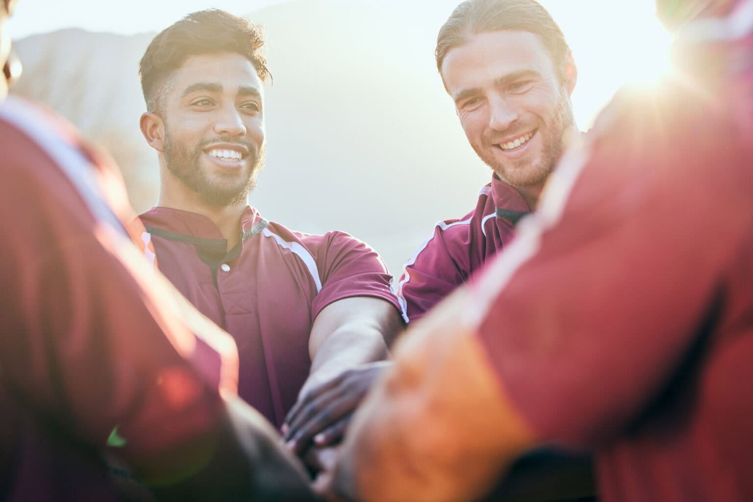 Smiling teammates stacking hands together in a sunlit huddle