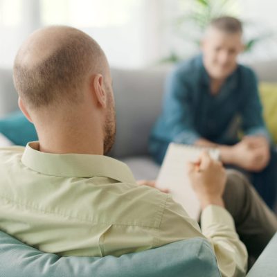 Professional therapist meeting a patient in his office, he is writing down notes and listening